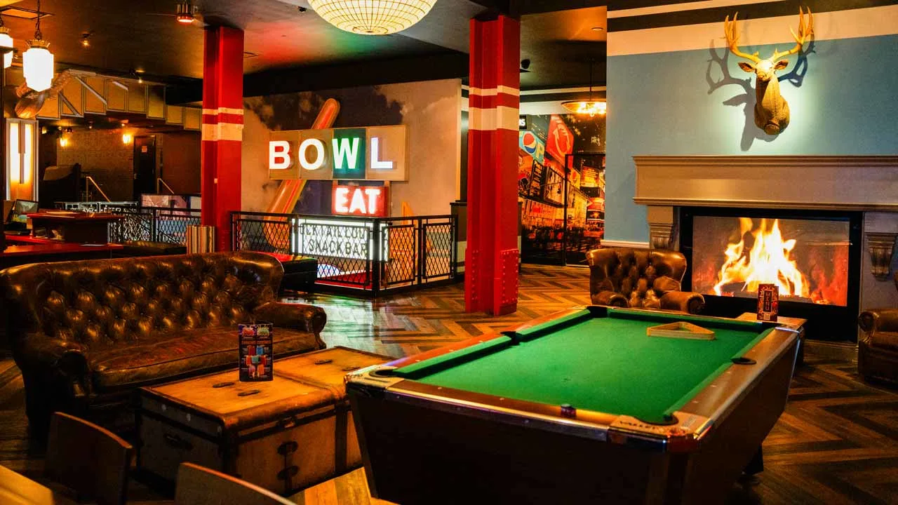 Pool table and full bar area inside Lucky Strike Times Square entertainment venue with globe pendant lighting and herringbone wood floors