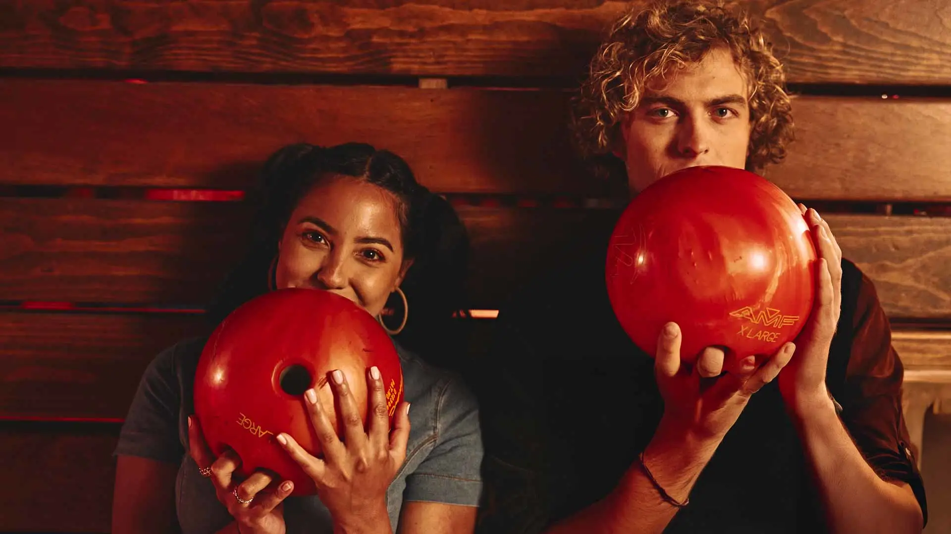 Couple holding bowling balls and smiling together in a stylish bowling alley.