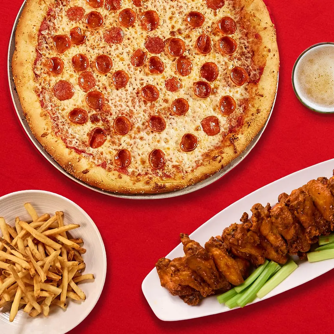 Delicious pepperoni pizza, crispy wings, and french fries on a red holiday-themed table.