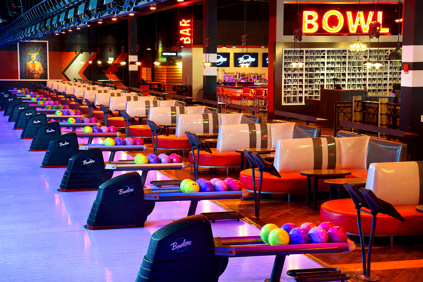 Colorful bowling balls on return rack with bowling center in the background.