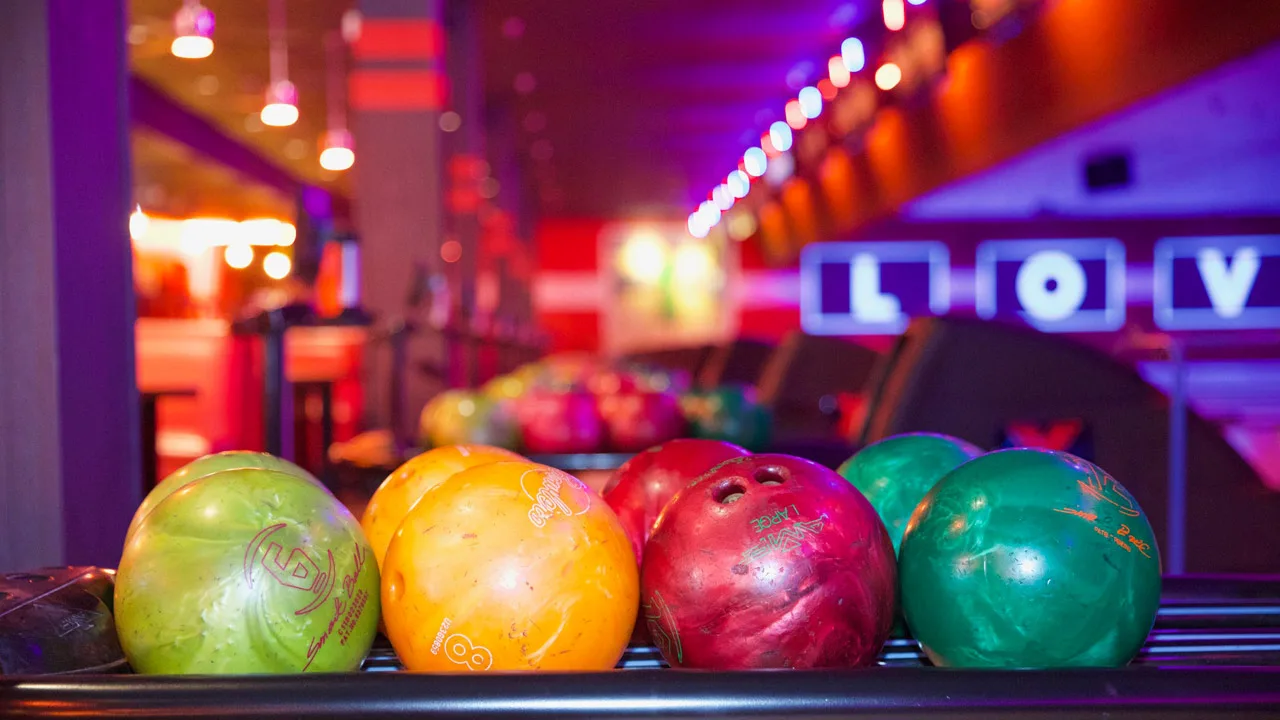 Colorful bowling balls in a return rack with a large bowling alley in the background.