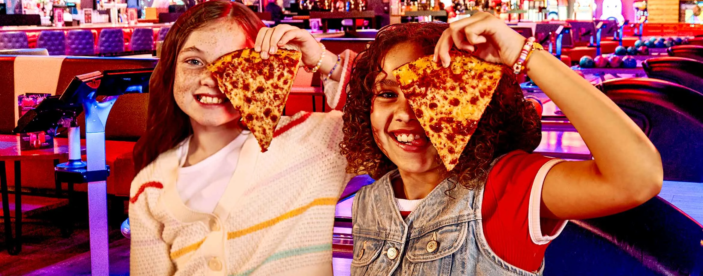 Two kids holding a slice of cheese pizza while at a bowling alley