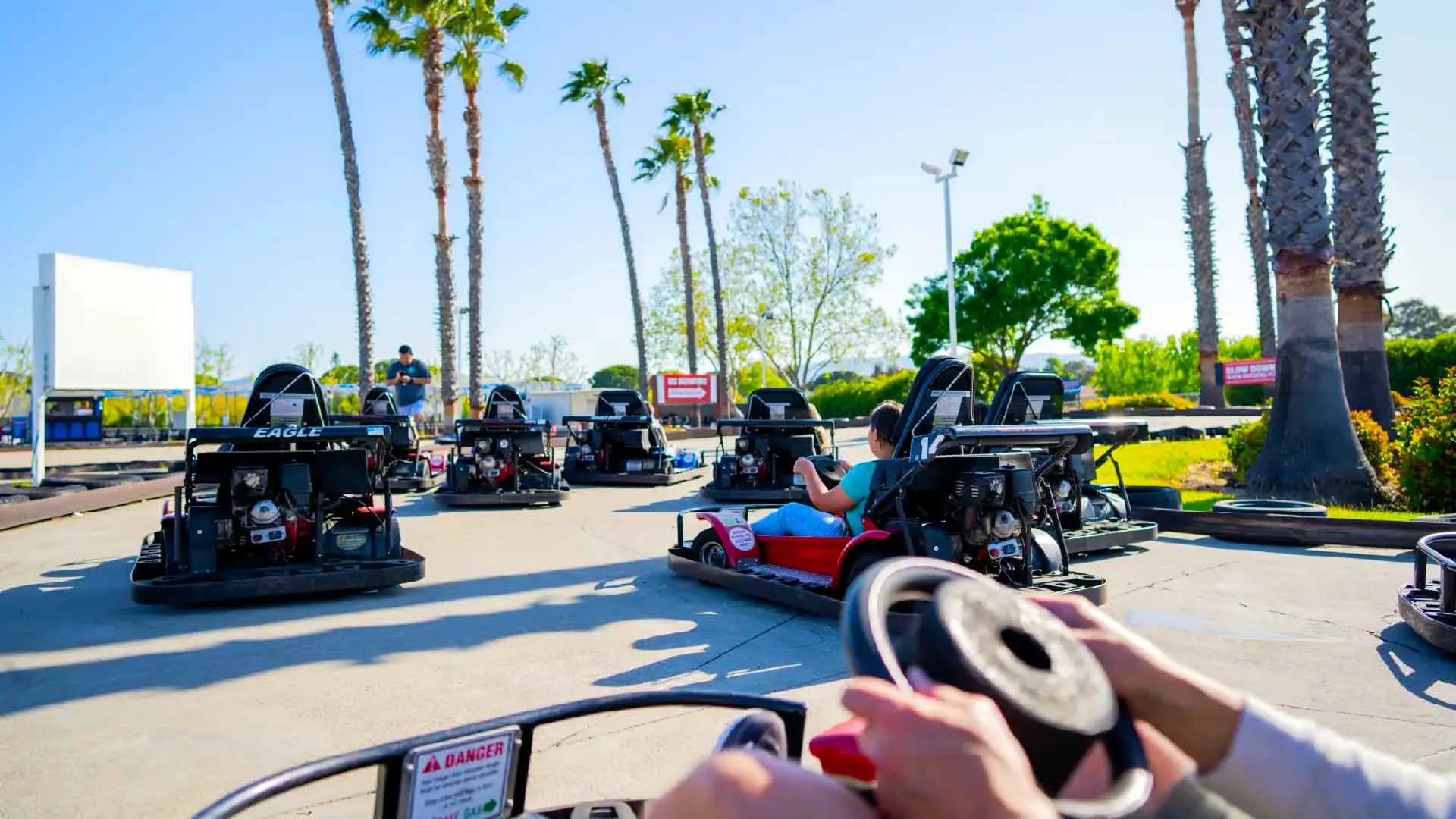 Guests racing go-karts on an outdoor track lined with palm trees at a family entertainment center.