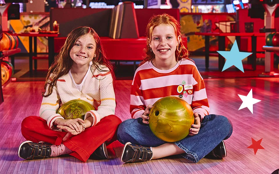 Two kids sitting on the floor by the bowling lanes