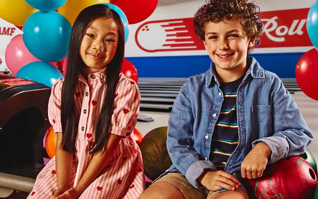 A boy and a girl sitting on top of a ball return machine at an AMF bowling center's kids party.