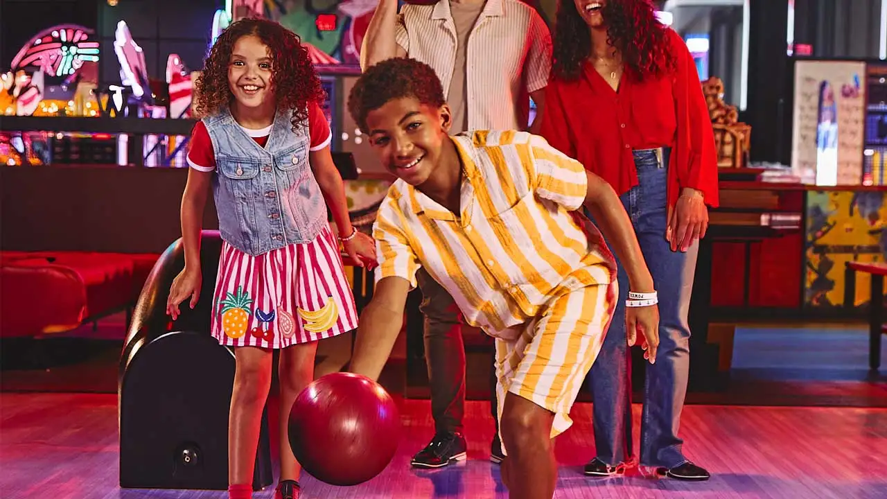 Family smiling and holding bowling balls together in a vibrant bowling center with neon lighting and a fun, welcoming atmosphere