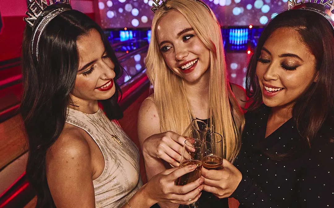 Friends toasting champagne on the bowling lanes at Lucky Strike during a New Year’s Eve party with festive lighting and celebration accessories.