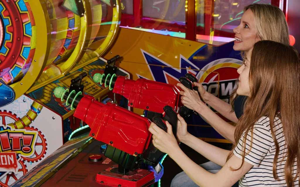 A mother and daughter smile and play a light-up arcade shooting game together in the AMF arcade.