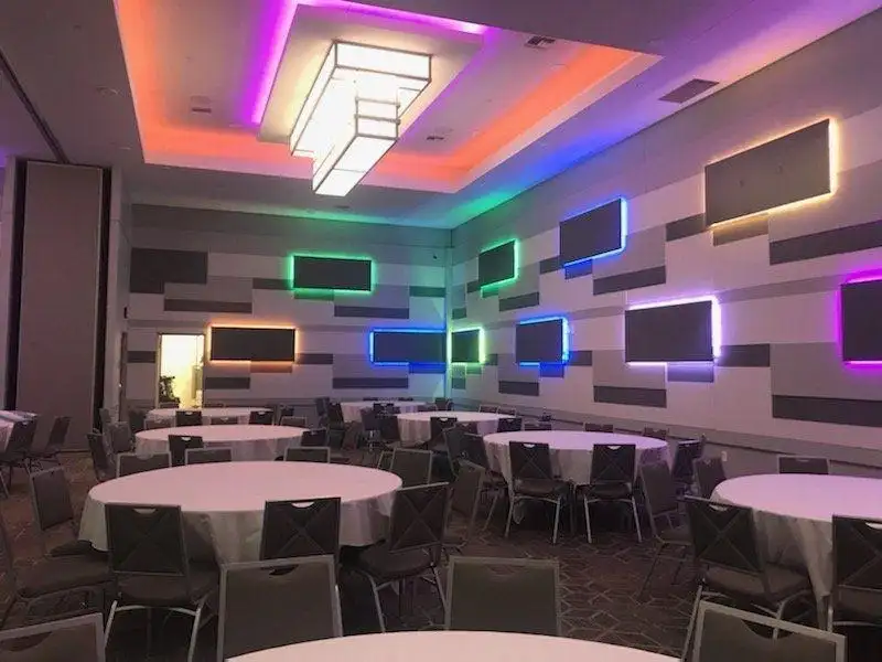 Large banquet room with several round tables covered in cloth and colorful lights on the walls