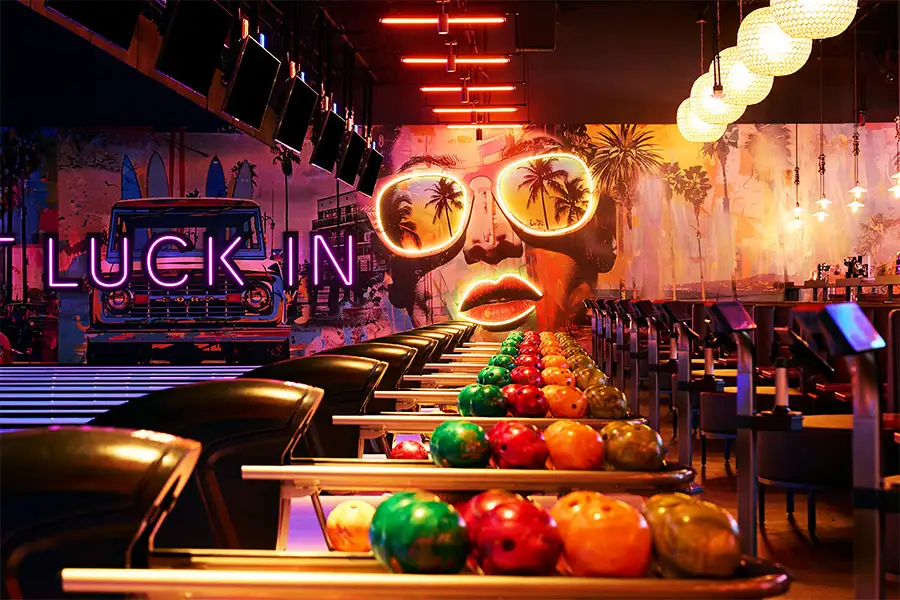 Colorful bowling ball on return rack with amazing bowling center and large mural in the background.