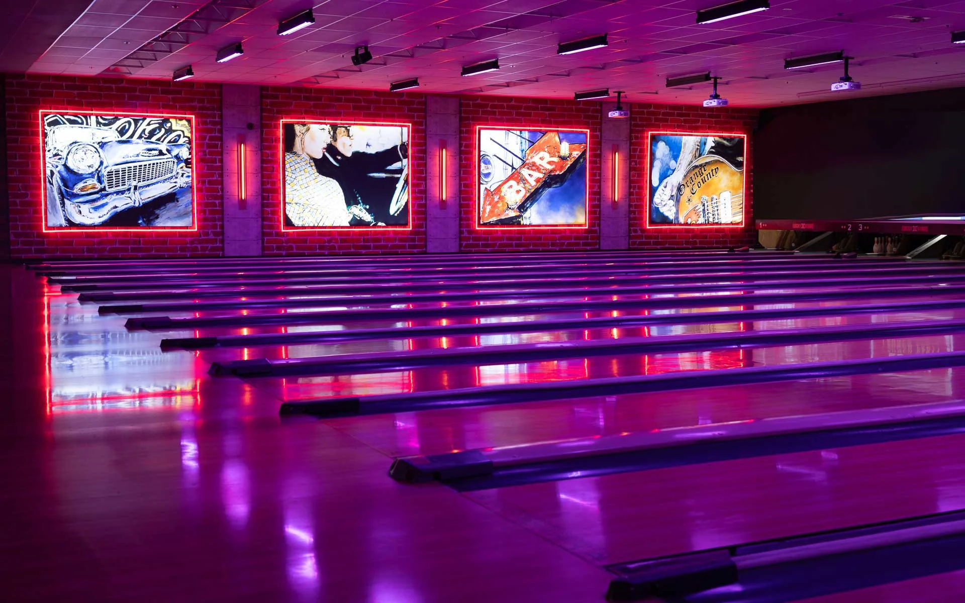 Moody bowling alley interior with pink and purple lighting, polished lanes, four illuminated wall murals, and digital screens above the pins.