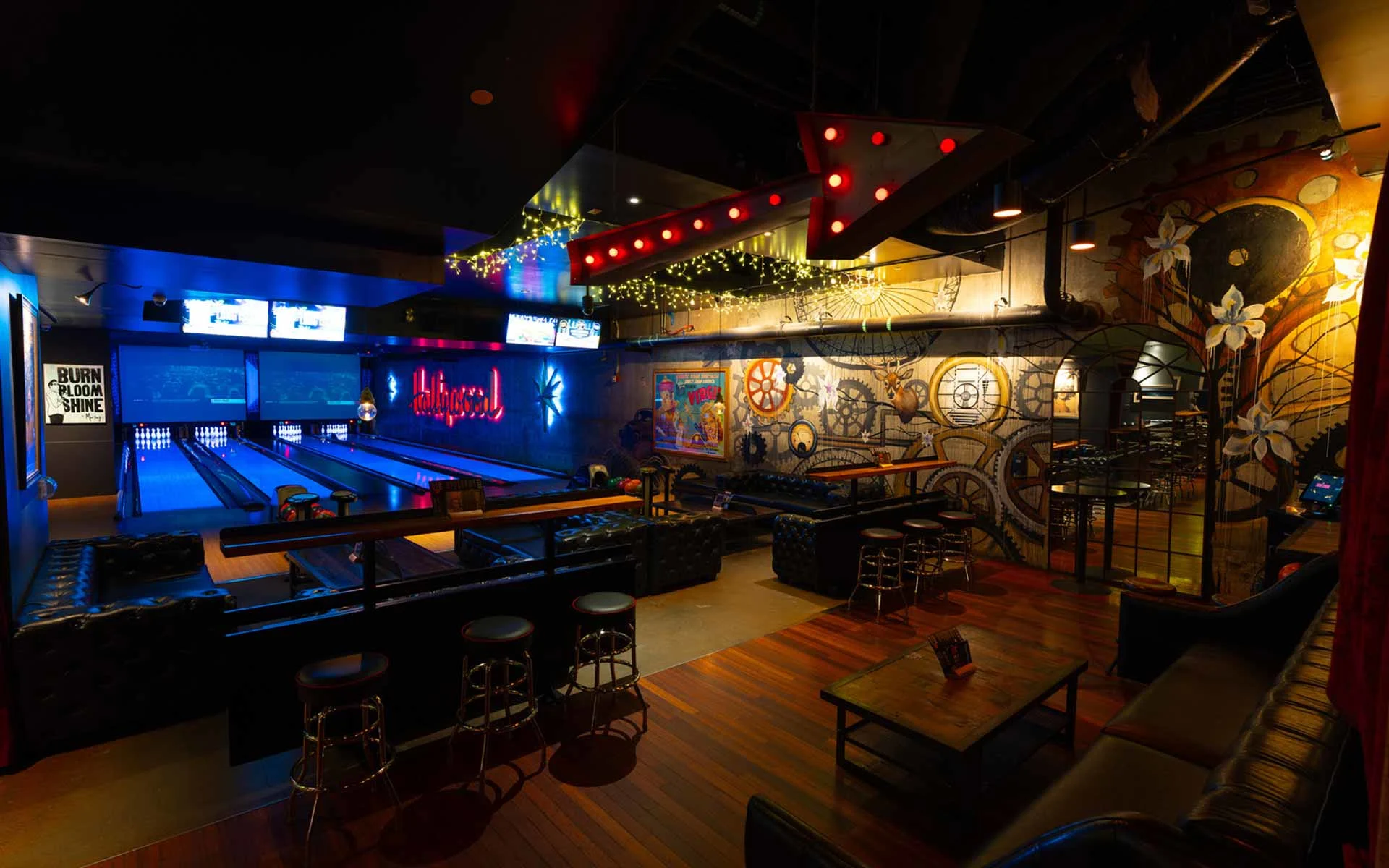 Stylish lane-side lounge featuring bold wall art, neon accents, and elevated seating. Combines a vibrant, artistic vibe with direct views of the lanes—ideal for groups looking for a more curated, social bowling experience.
