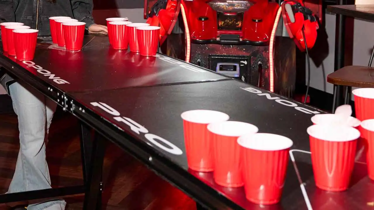 A neon-lit beer pong table set up inside a modern bowling entertainment venue.