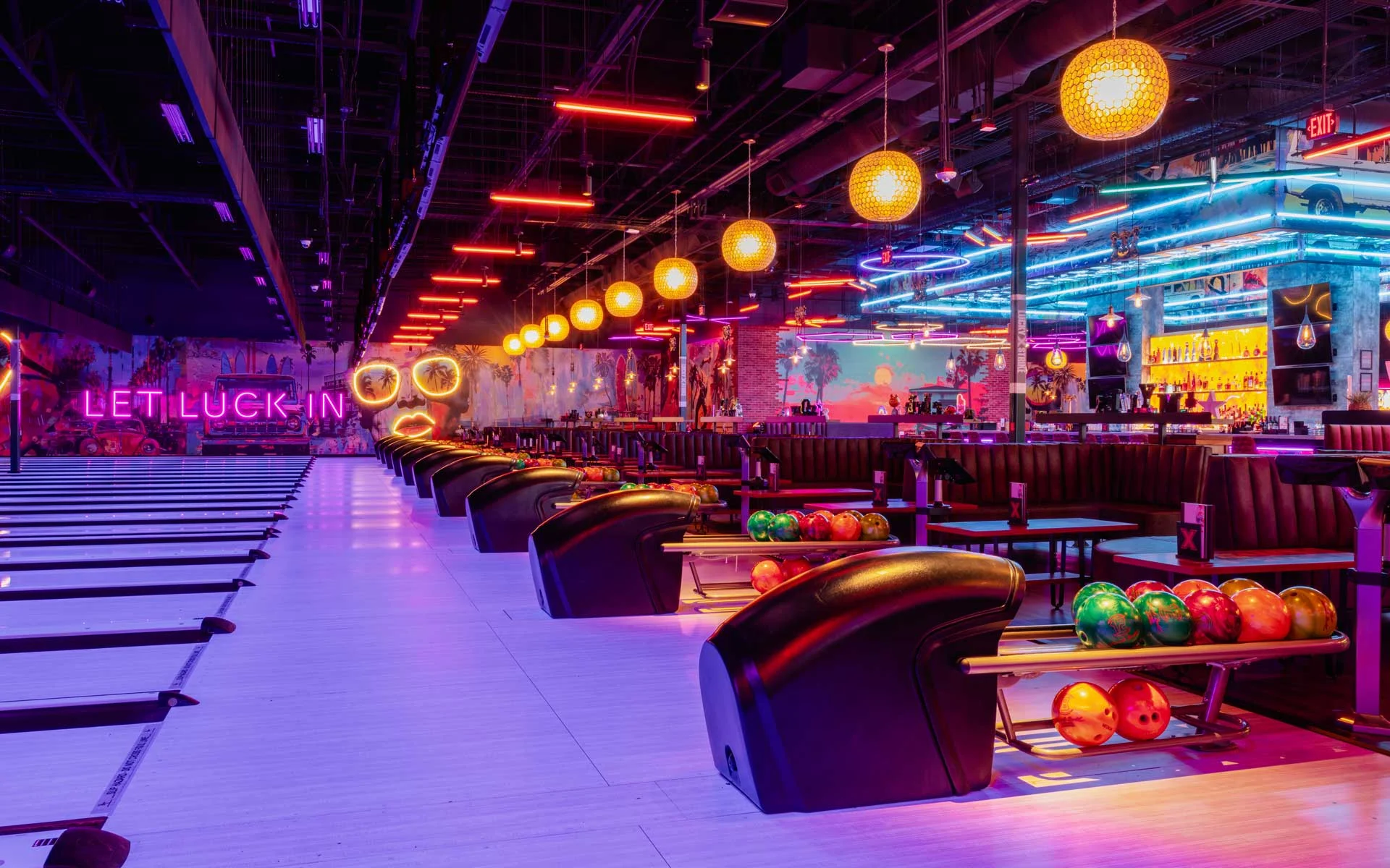 Modern bowling lanes with colorful neon lighting, seating areas with bowling balls and lounge chairs, and a vibrant upscale entertainment atmosphere at a Lucky Strike venue.