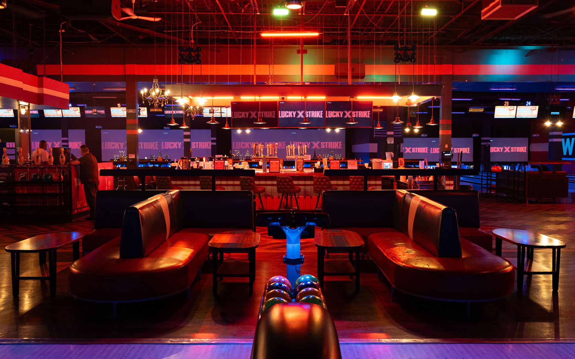 Modern lounge seating area with leather booths overlooking bowling lanes and a glowing Lucky Strike bar in the background.