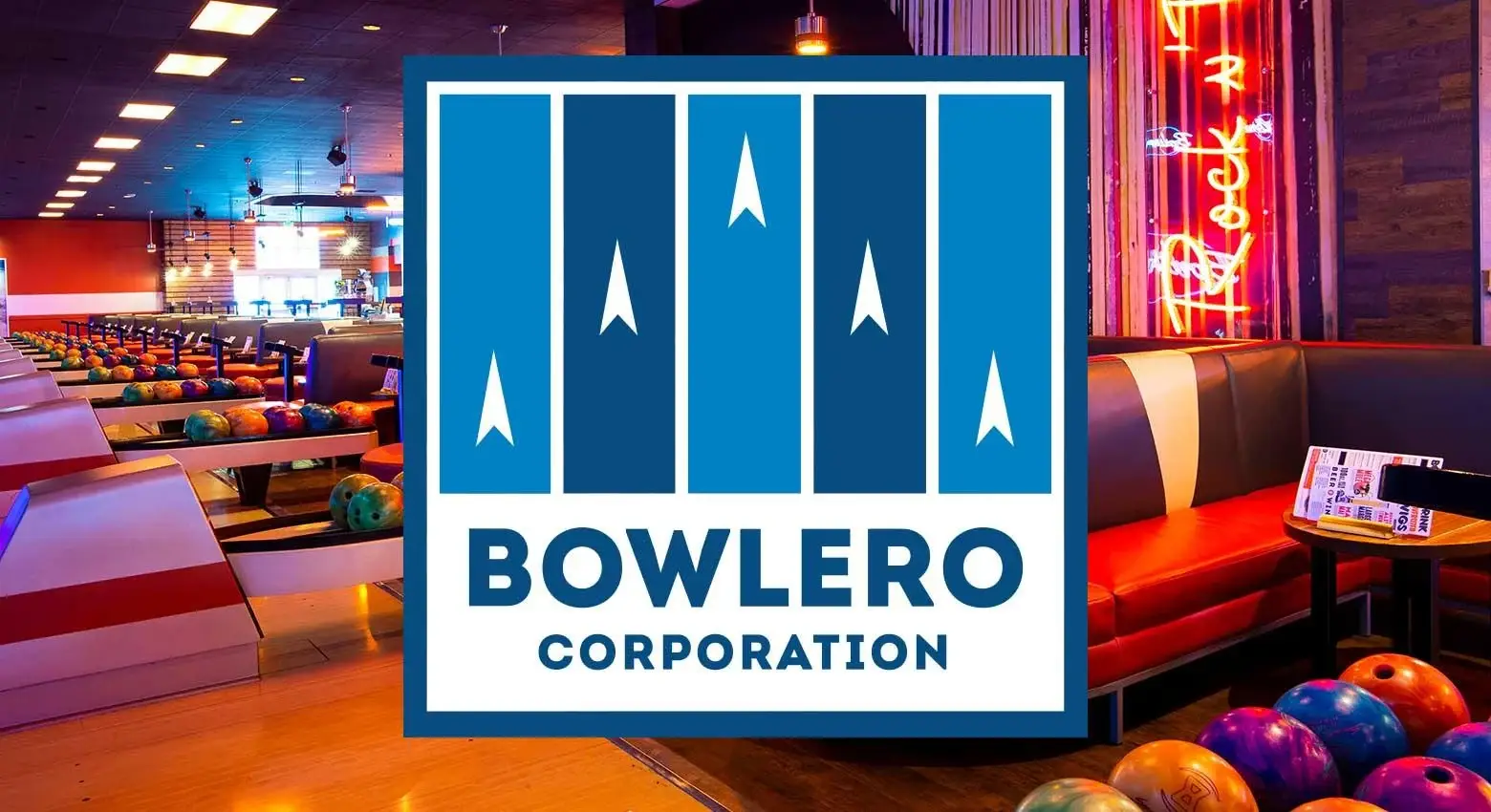 Modern bowling alley interior with colorful lanes, neon lighting, lounge seating, and bowling balls lined up beside the lanes.
