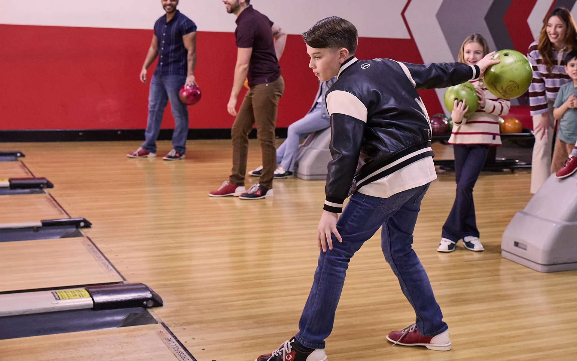 Young boy preparing to bowl while families and kids gather behind him at a lively bowling center, with lanes and equipment visible.