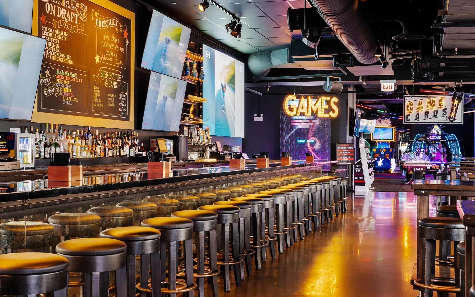 Full-service bar with TVs, stools, and nearby arcade games in a vibrant Lucky Strike entertainment venue.