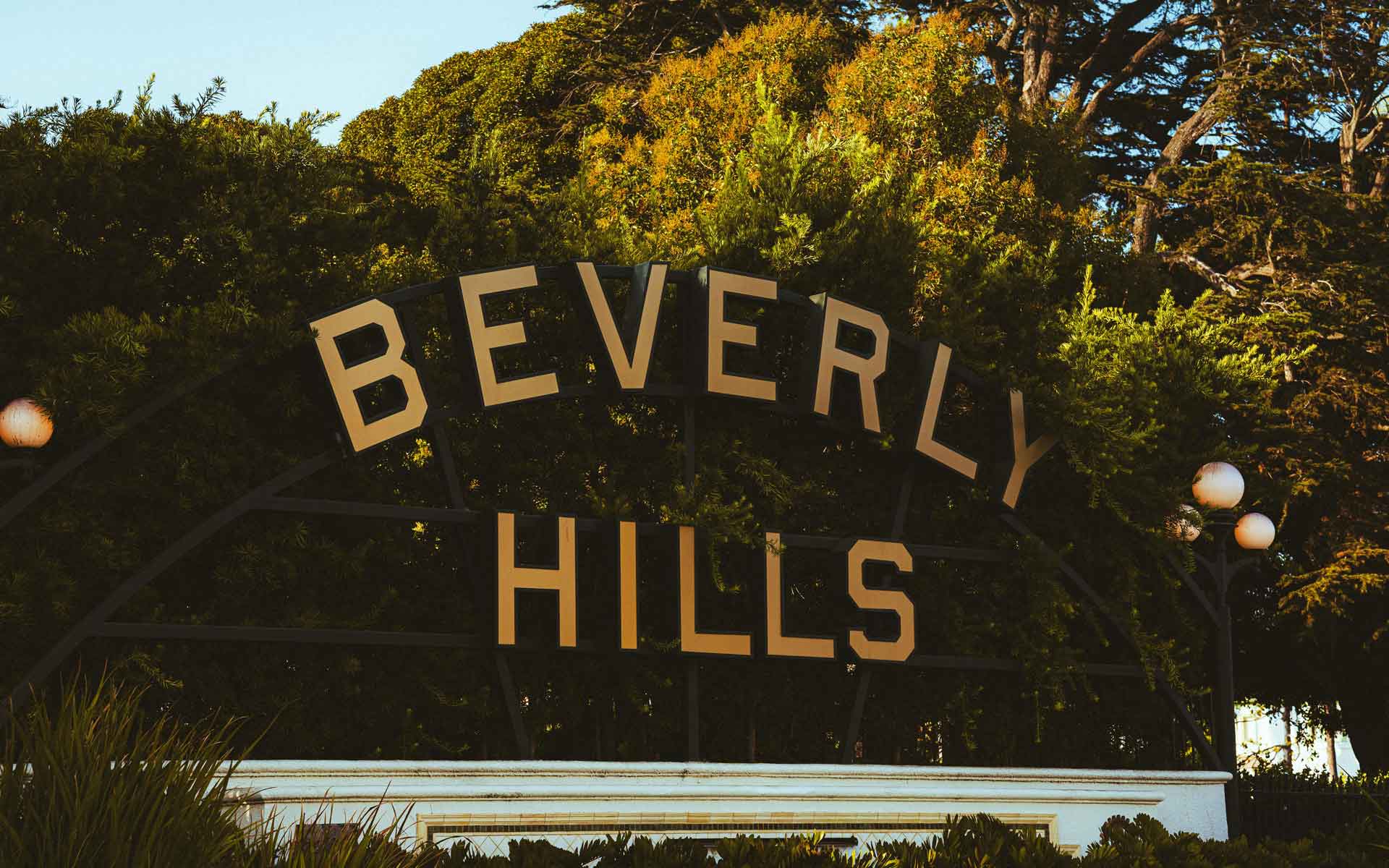 Beverly Hills sign at Beverly Gardens Park surrounded by trees at golden hour.