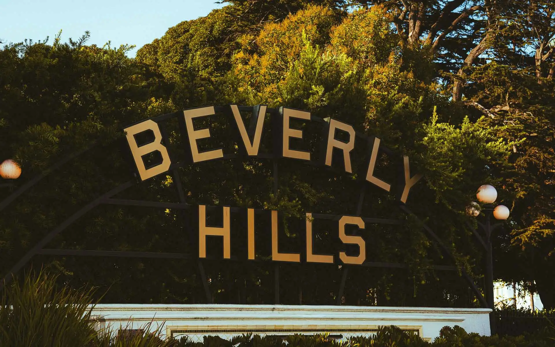 Beverly Hills sign at Beverly Gardens Park surrounded by trees at golden hour.