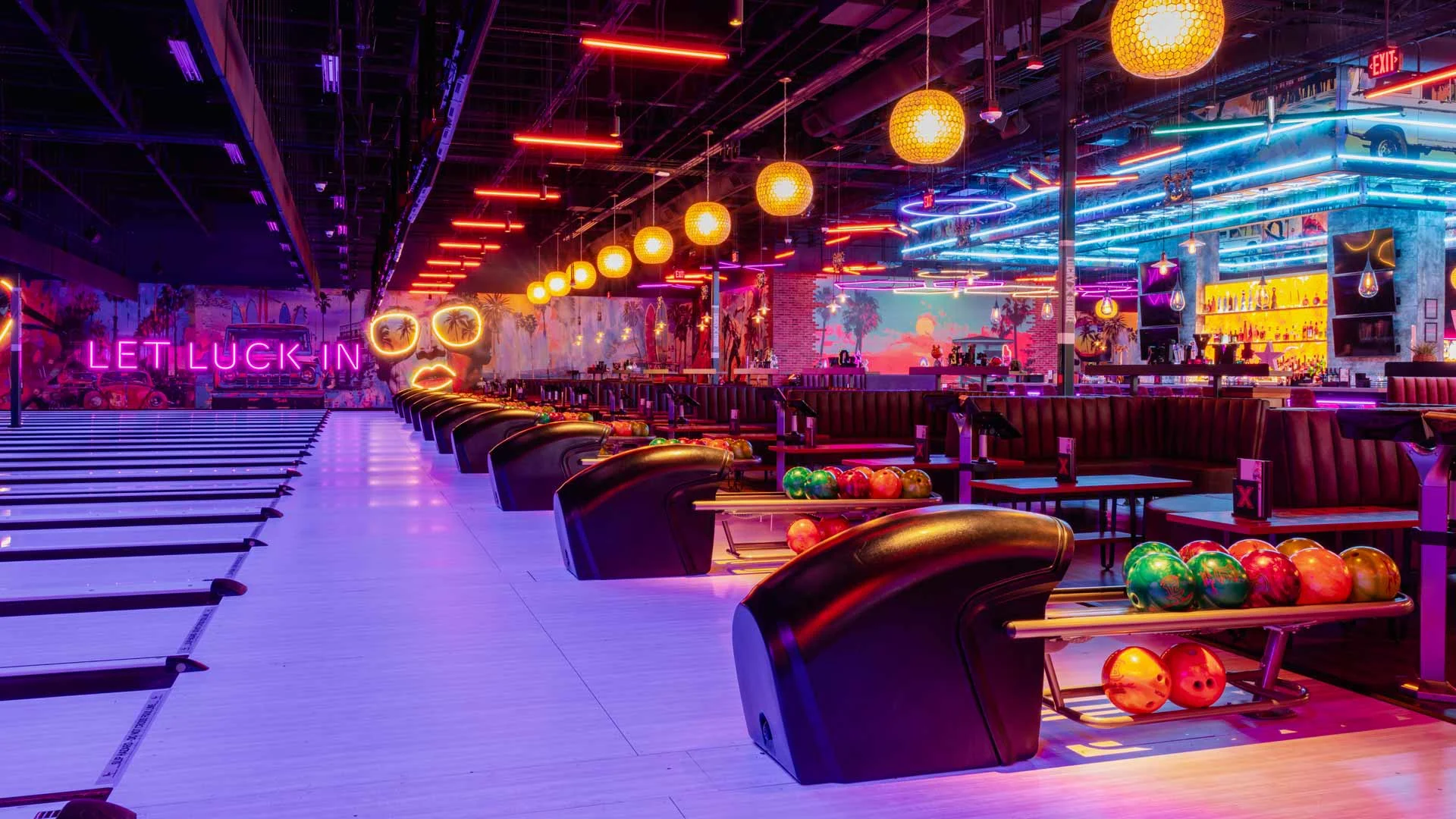 Upscale bowling lanes with lounge seating and colorful "Let Luck In" neon lighting at a modern entertainment venue.