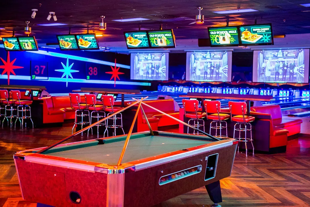 Billiards table with bar and large TV screens in the background