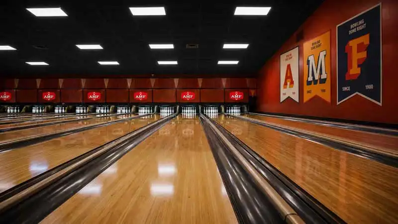 Multiple bowling lanes at an AMF bowling center, viewed from the approach with pins set at the end and AMF logos displayed above each lane.