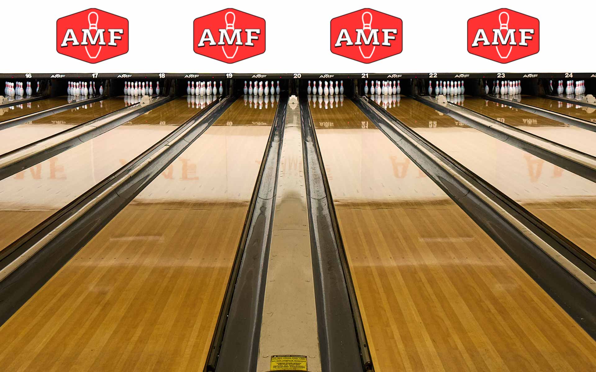 Multiple bowling lanes at an AMF bowling center, viewed from the approach with pins set at the end and AMF logos displayed above each lane.