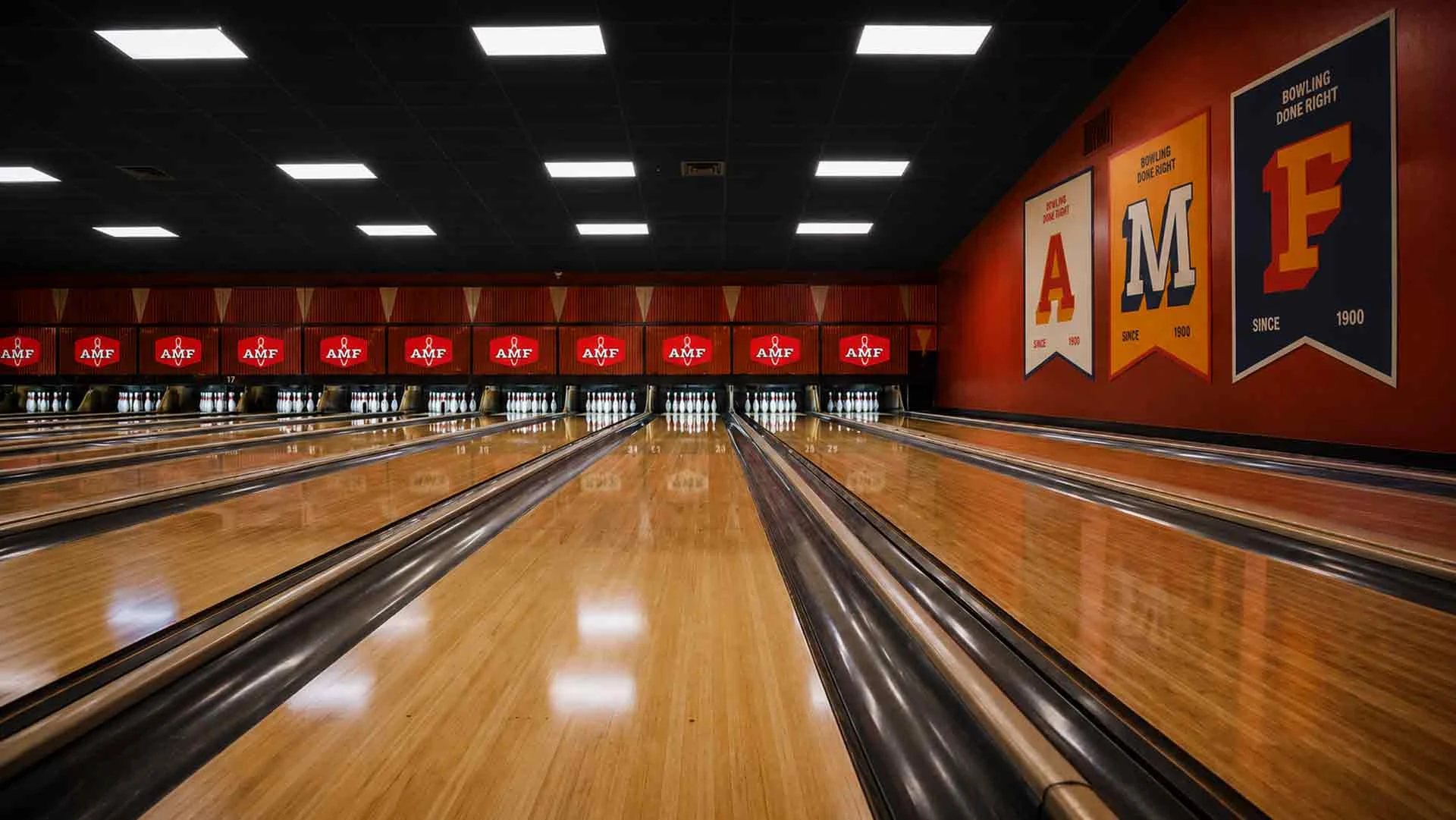 Multiple bowling lanes at an AMF bowling center, viewed from the approach with pins set at the end and AMF logos displayed above each lane.