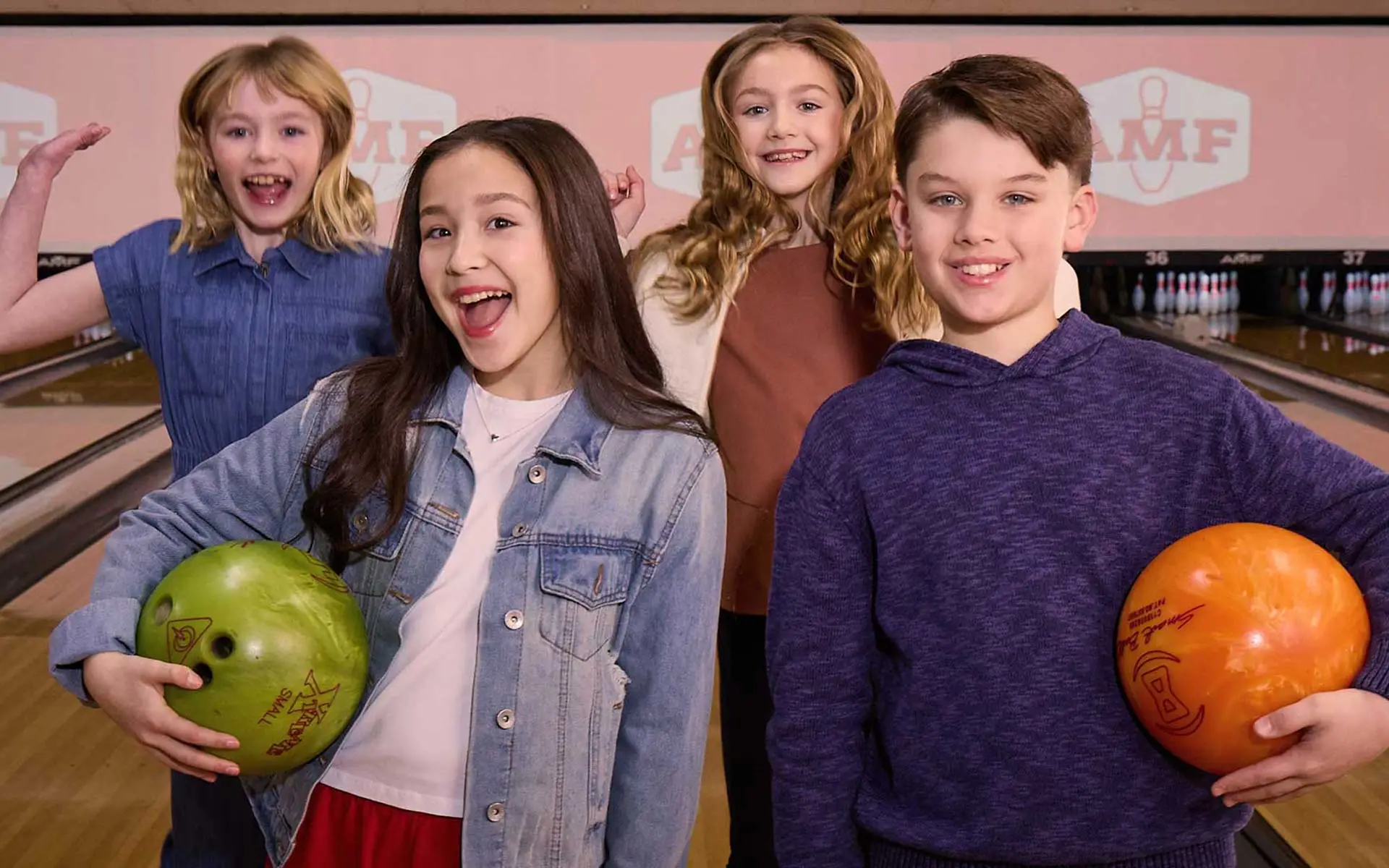 Group of four kids smiling and holding bowling balls while standing on a bowling lane at an AMF bowling center.