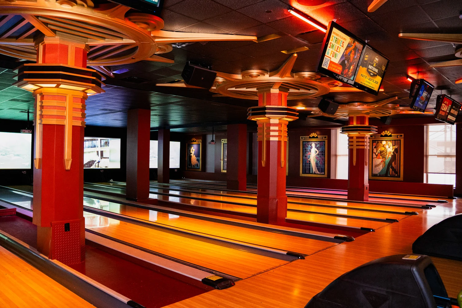 Wide view of bowling lanes at Lucky Strike Times Square featuring Art Deco columns, warm amber lighting, and overhead scoring screens