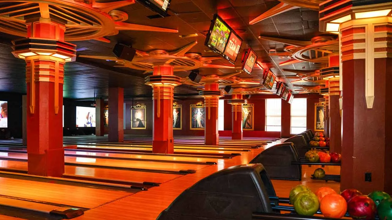 Wide view of bowling lanes at Lucky Strike Times Square featuring Art Deco columns, warm amber lighting, and overhead scoring screens