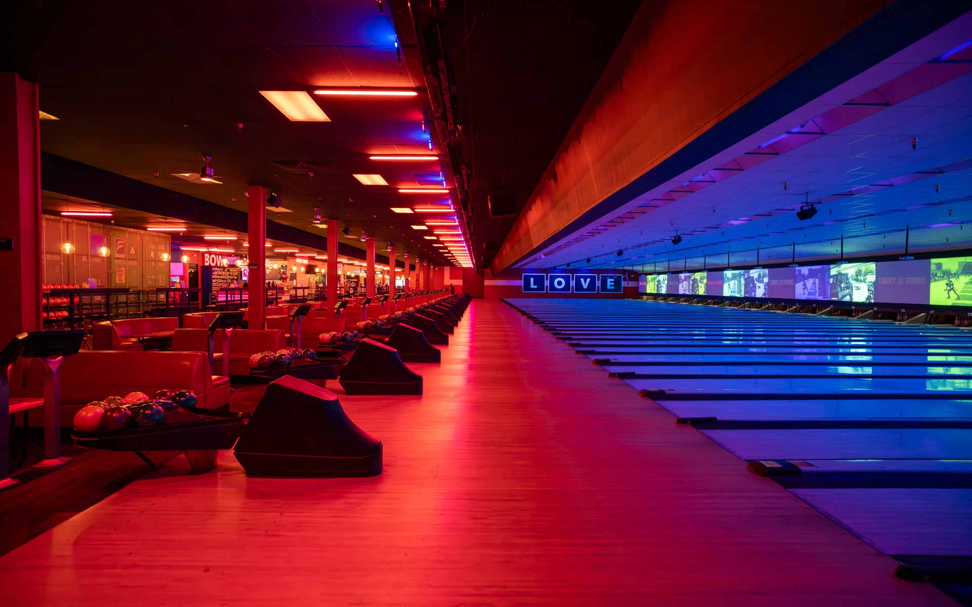 Expansive bowling lanes at Lucky Strike with dramatic red and blue lighting, scoring screens, and a sleek, modern layout.