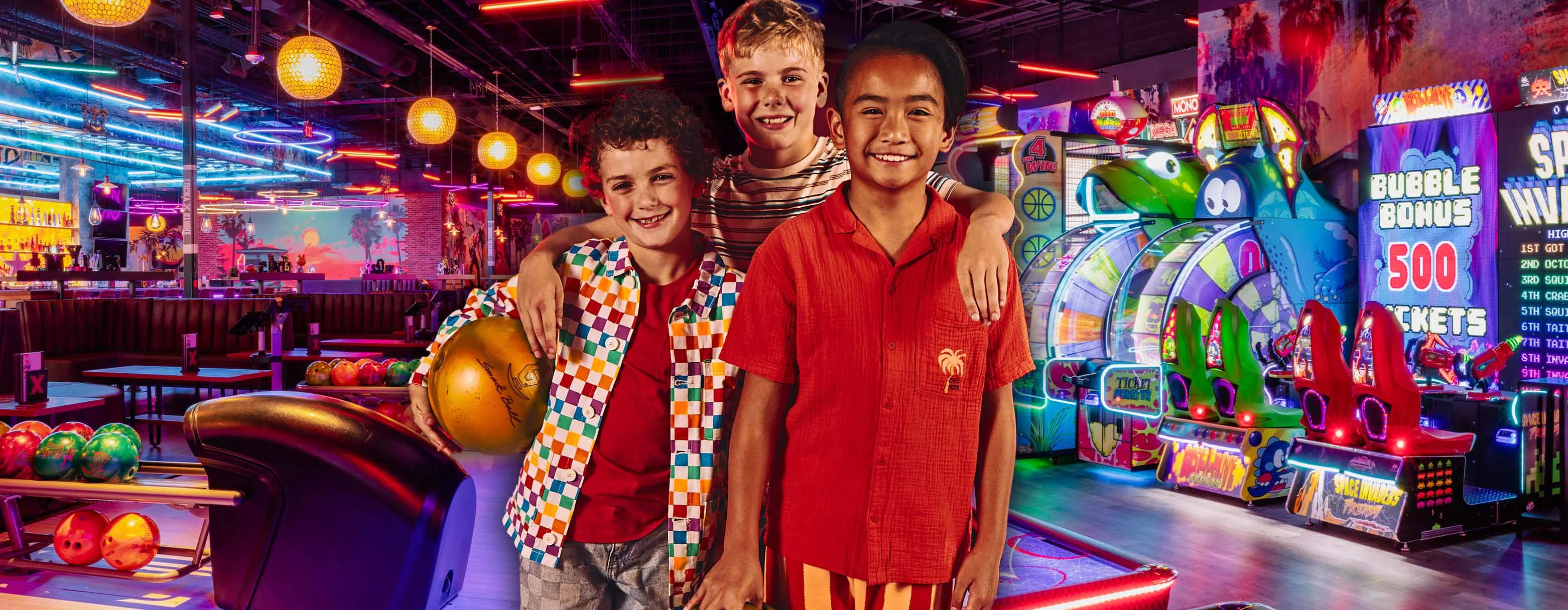 Three kids with a colorful bowling center and arcade in the background.