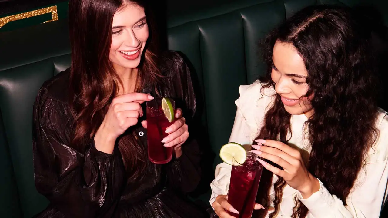Two women drinking cocktails at a Lucky Strike center lane approach booth.