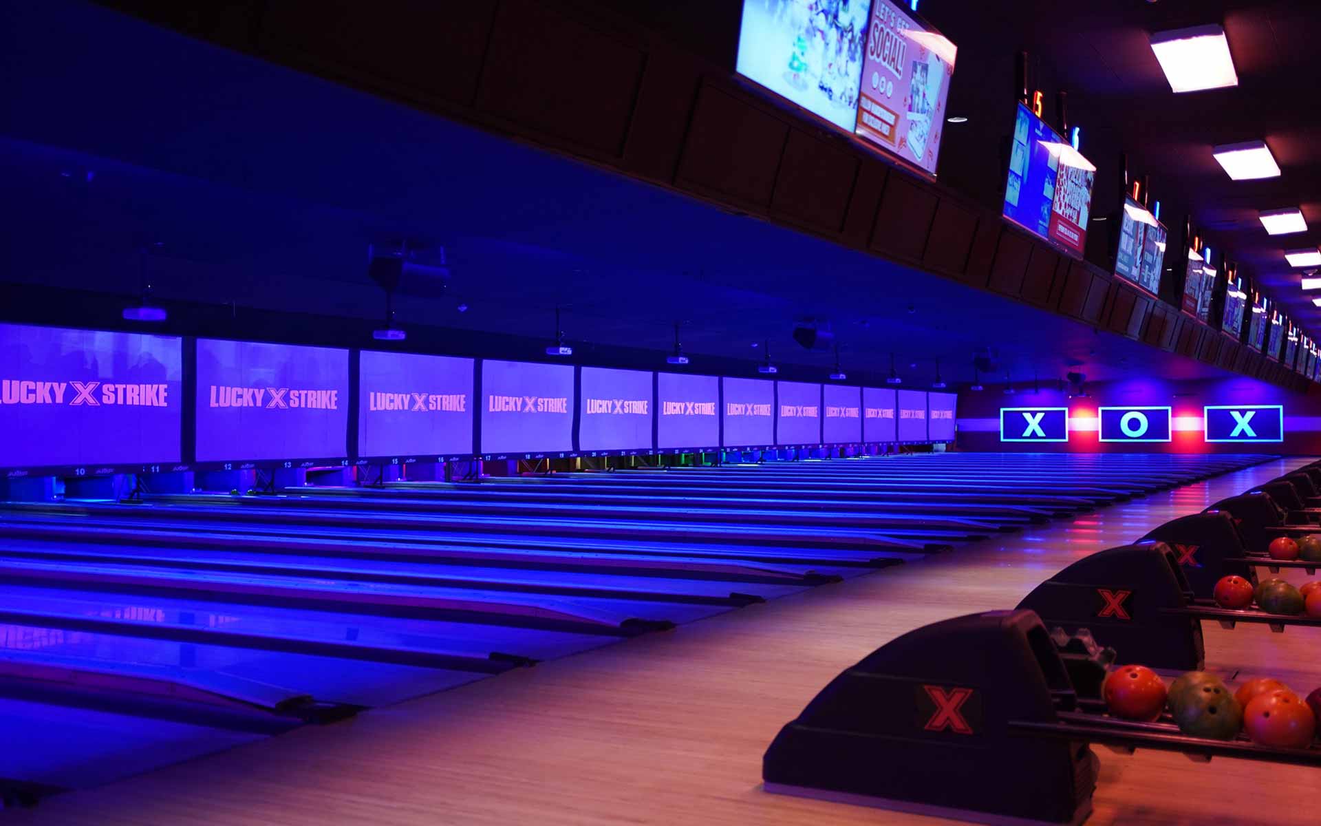 Sleek bowling lanes at Lucky Strike illuminated with blue and purple lighting, overhead scoring screens, and modern design.