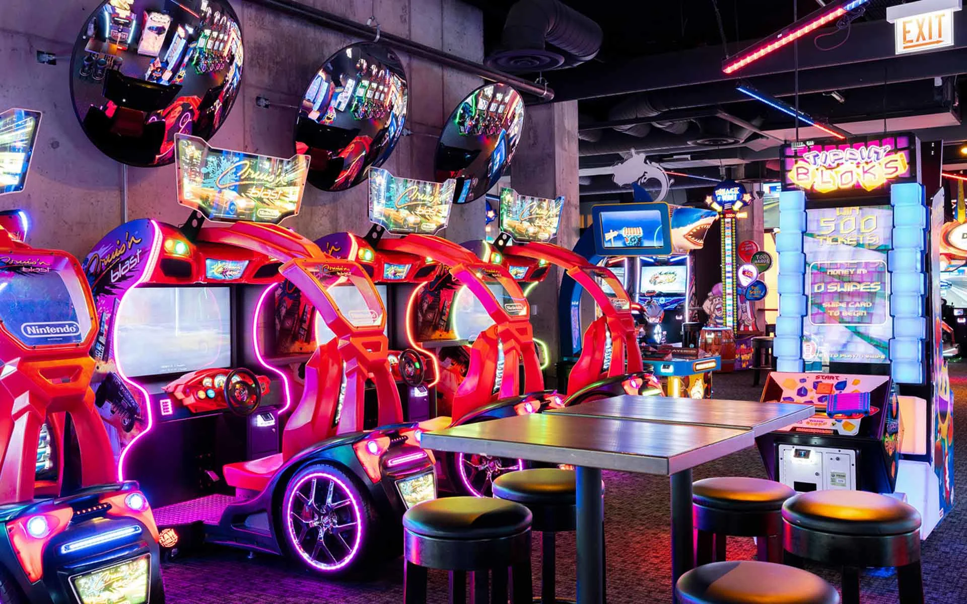 Neon-lit arcade at Lucky Strike featuring red racing simulators, colorful LED lighting, and modern video game machines in an upscale entertainment venue.