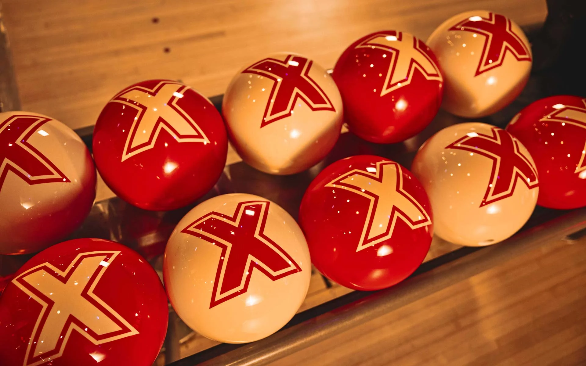 Row of red and cream Lucky Strike bowling balls lined up on a rack inside a bowling center.
