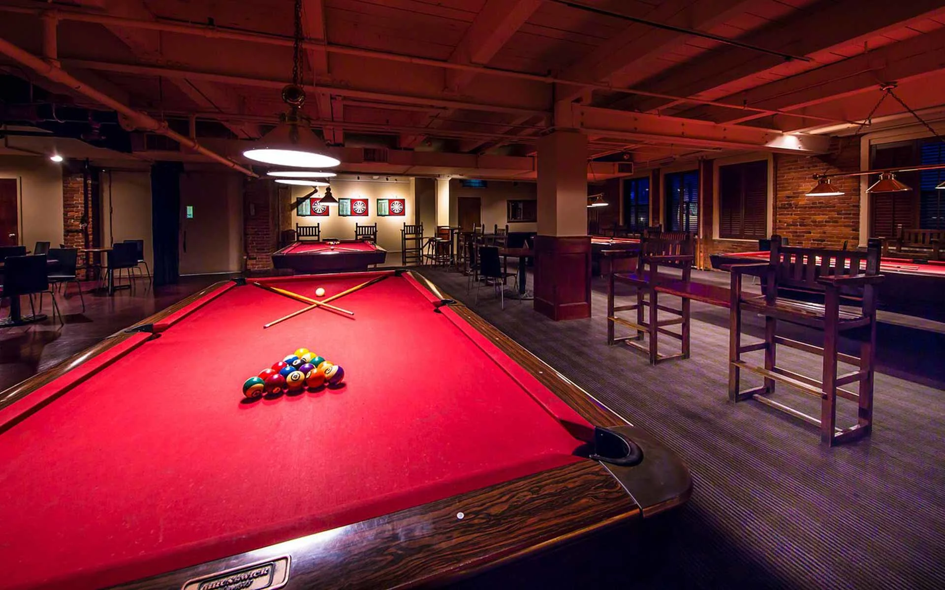 Upscale billiards lounge with red felt pool tables, cue racks, and warm ambient lighting in a stylish entertainment setting.