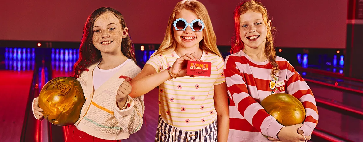 Three girls with in front of bowling lanes, the girl in the middle is holding a Summer Season Pass