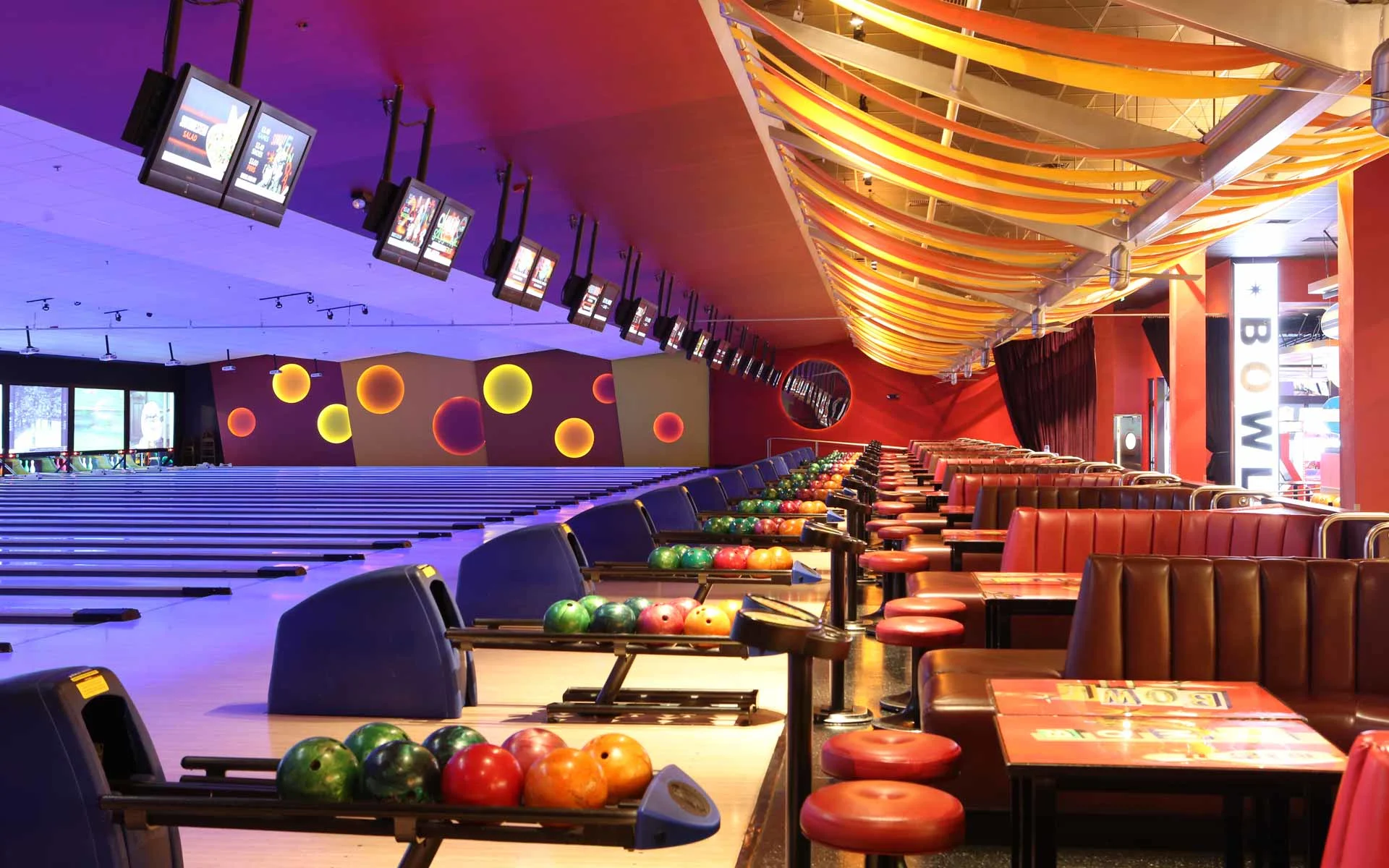 Bowling lanes with vibrant lighting, scoring screens, and lane-side seating in a high-energy Bowlero entertainment venue