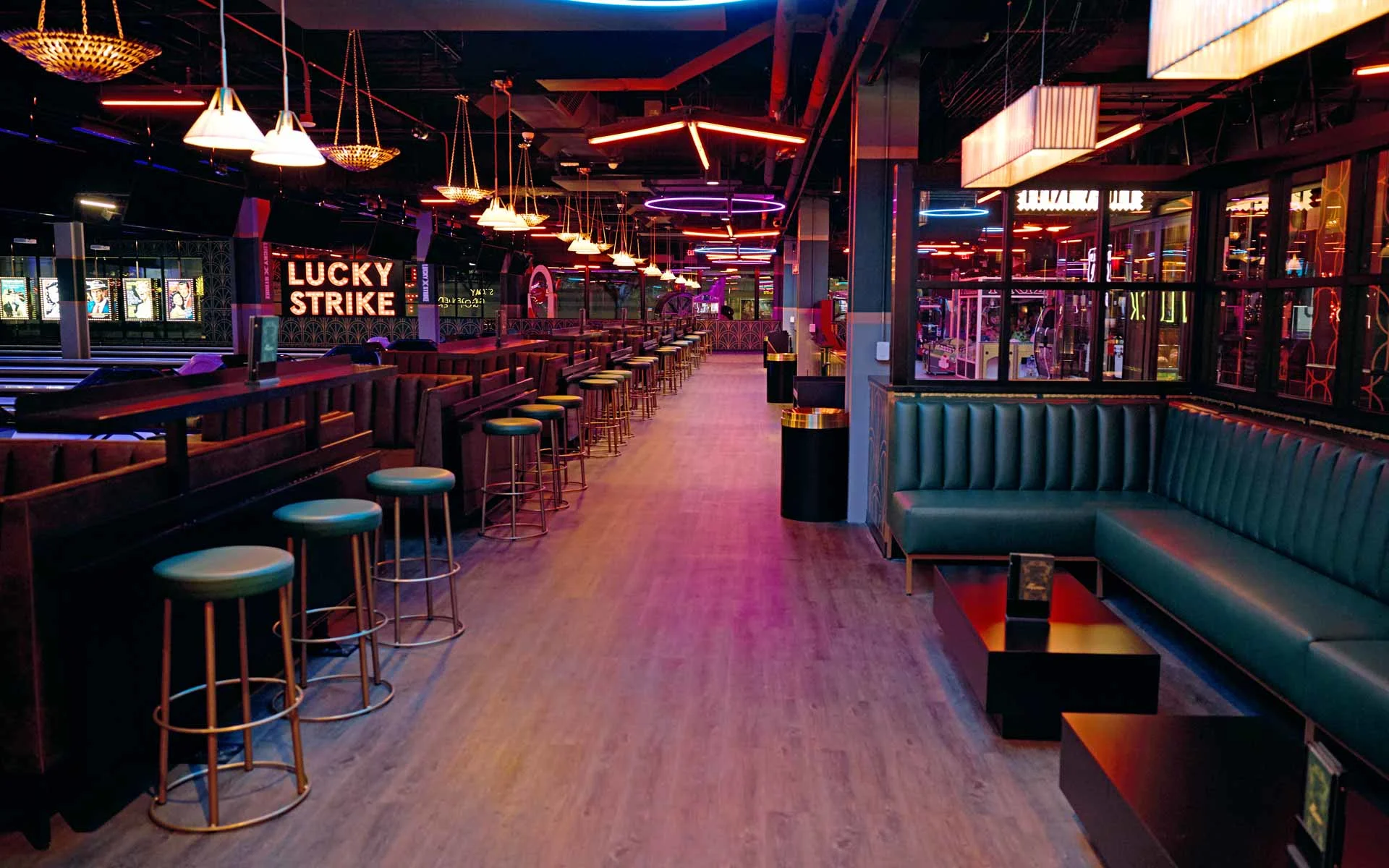 Modern upscale bowling lounge interior with neon lighting, leather booth seating, bar stools, and bowling lanes at a Lucky Strike venue, featuring a vibrant nightlife atmosphere with arcade elements and illuminated signage.