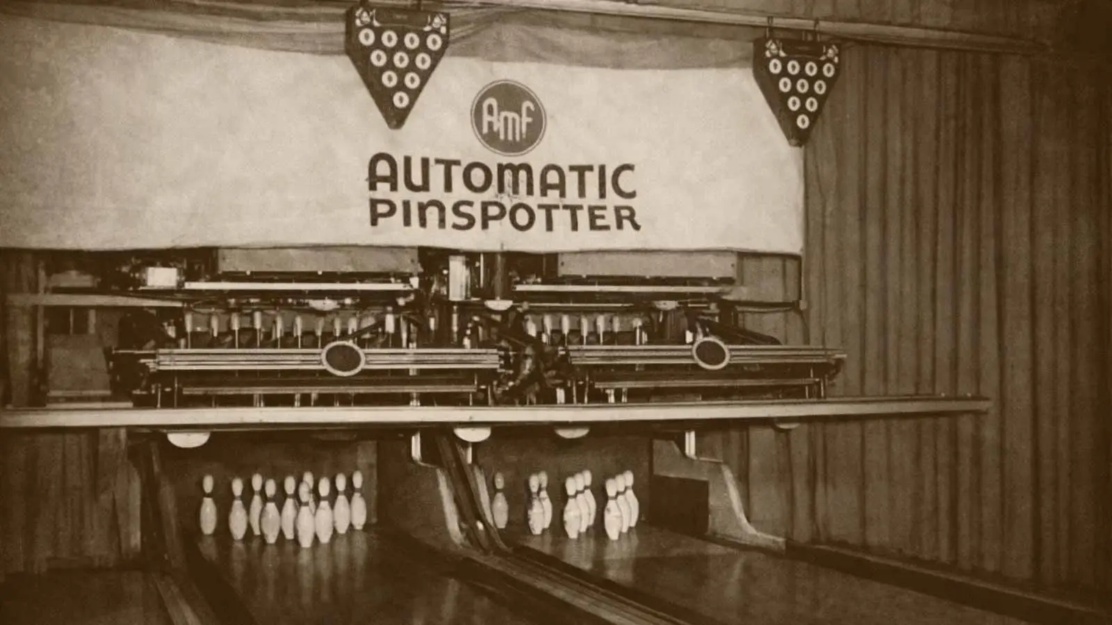 Vintage sepia-toned image of an AMF Automatic Pinspotter machine above bowling lanes with pins set beneath the mechanical equipment.