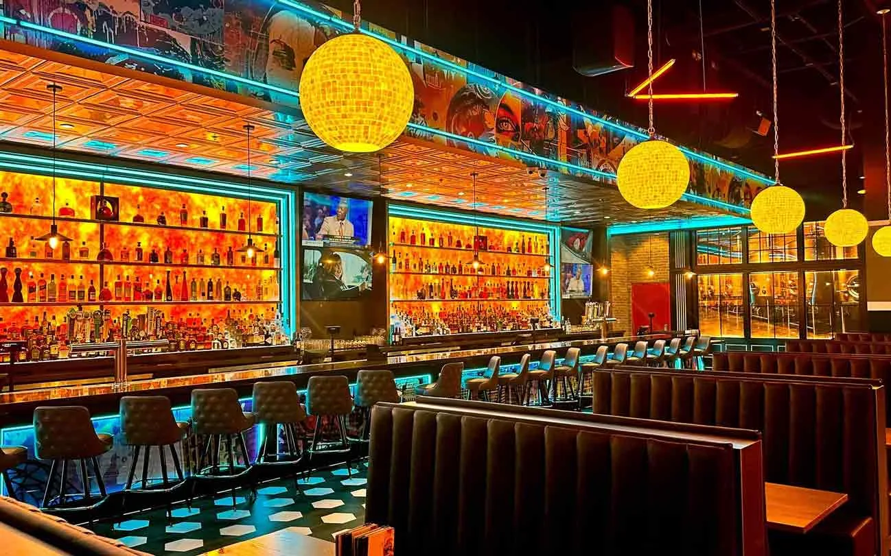 Full back bar with amber-lit liquor shelves, globe pendant lights, and mural ceiling at Lucky Strike Southlands.