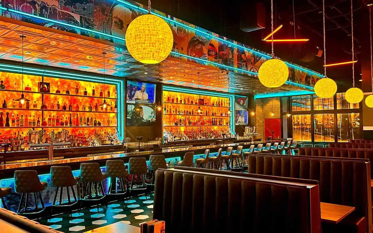 Full back bar with amber-lit liquor shelves, globe pendant lights, and mural ceiling at Lucky Strike Southlands.