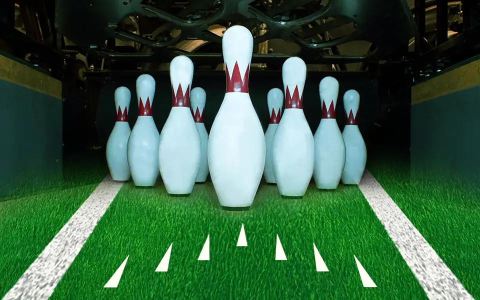 Bowling pins on a bowling lane displaying arrows and resting on football turf.