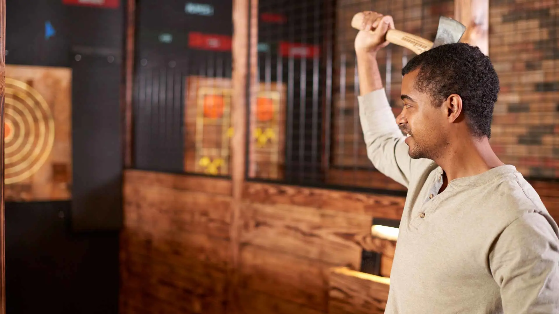 Man preparing to throw an axe in an indoor axe-throwing lane, standing in front of wooden targets in a rustic entertainment venue.