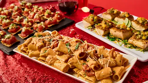 Holiday catering spread at Lucky Strike featuring pasta, seared fish, and assorted hors d’oeuvres on a festive red table.