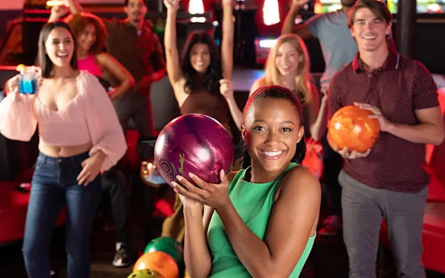 Girl holding a bowling ball with friends behind her.