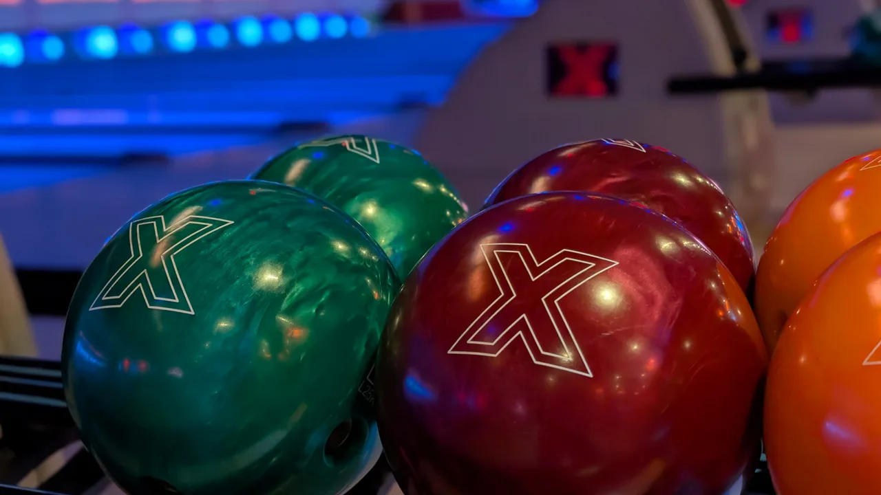 Close-up shot of colorful bowling balls in a return rack with black light bowling lanes in the background.